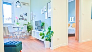 Een moderne woonkamer met een eethoek, een televisie en verschillende kamerplanten.
