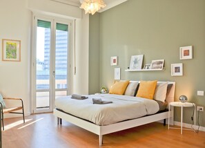 A bedroom with a bed, a bedside table, a chair, and a window with a view of buildings.