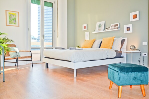 A modern bedroom with a bed, a side table, a chair, and a small ottoman.