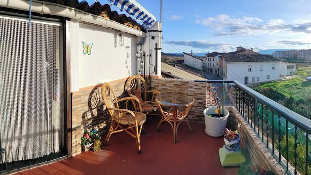 Un balcon avec des fauteuils en osier, une table et des plantes en pot.