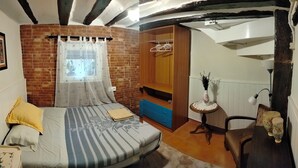Une chambre avec un mur en briques, un lit avec une literie à rayures, une armoire en bois, une petite table avec un vase et une chaise.