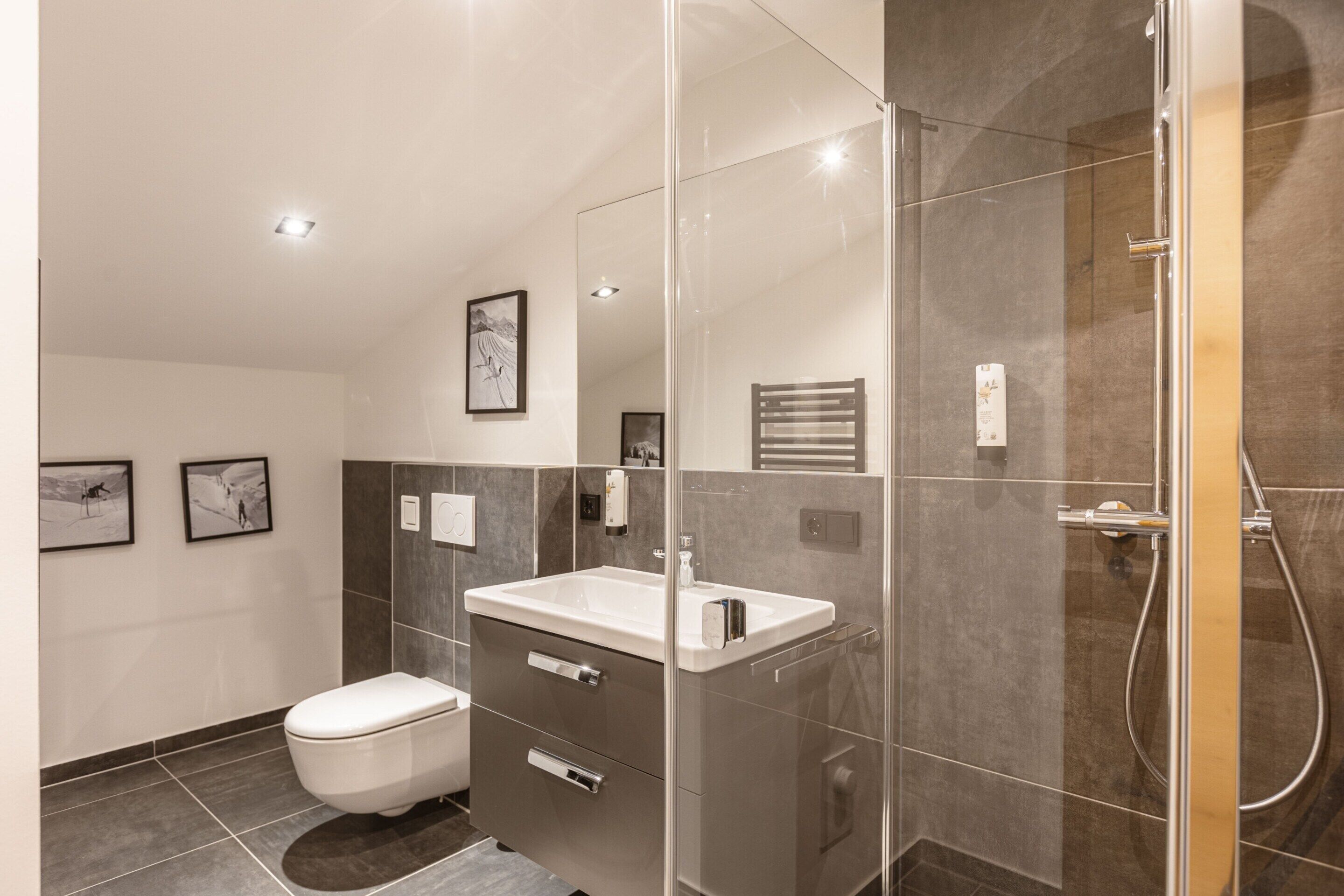 Een moderne badkamer met een douchecabine van glas, een witte wastafel en een toilet.