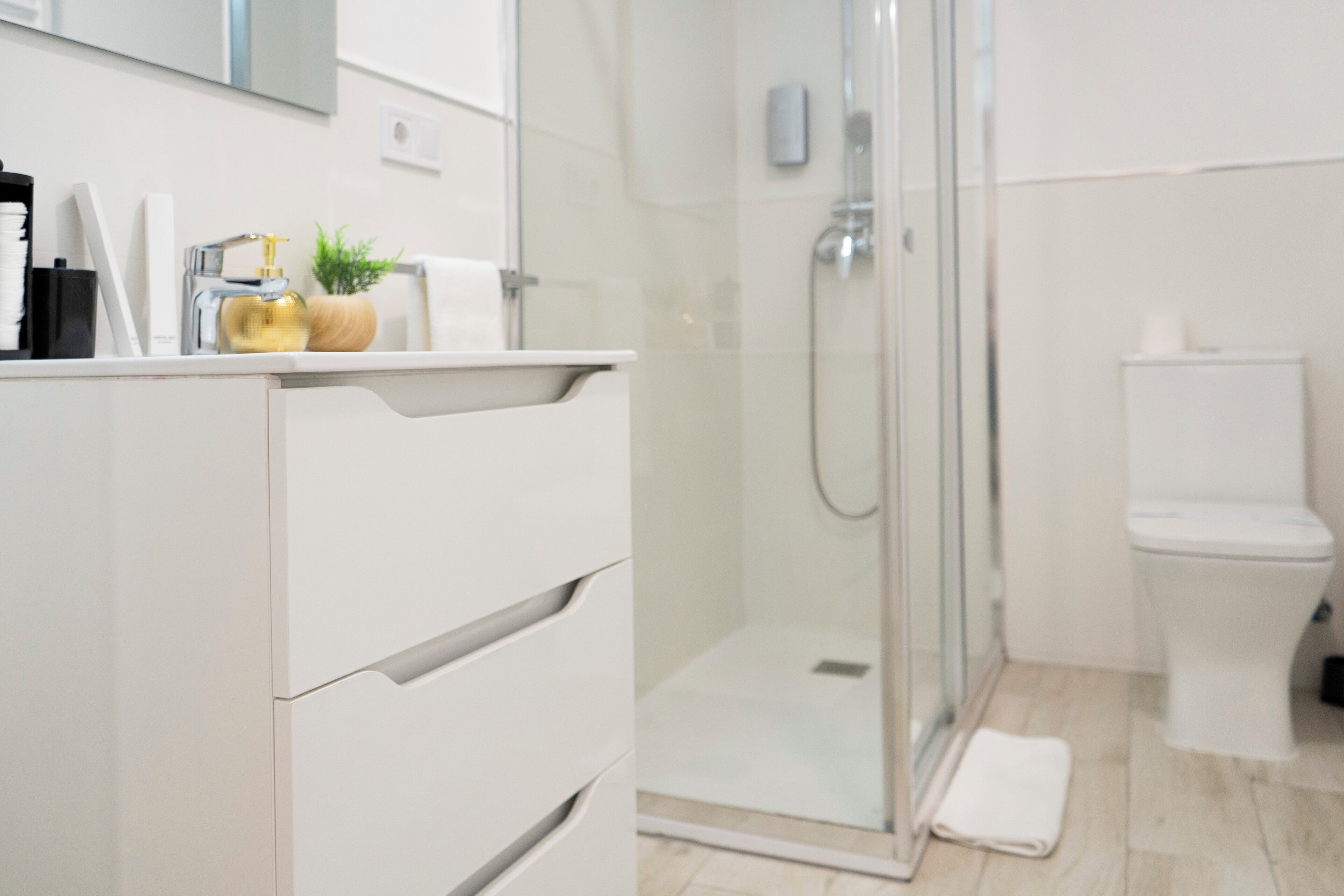 Un baño moderno con cabina de ducha de vidrio, inodoro blanco y tocador con una botella dorada.