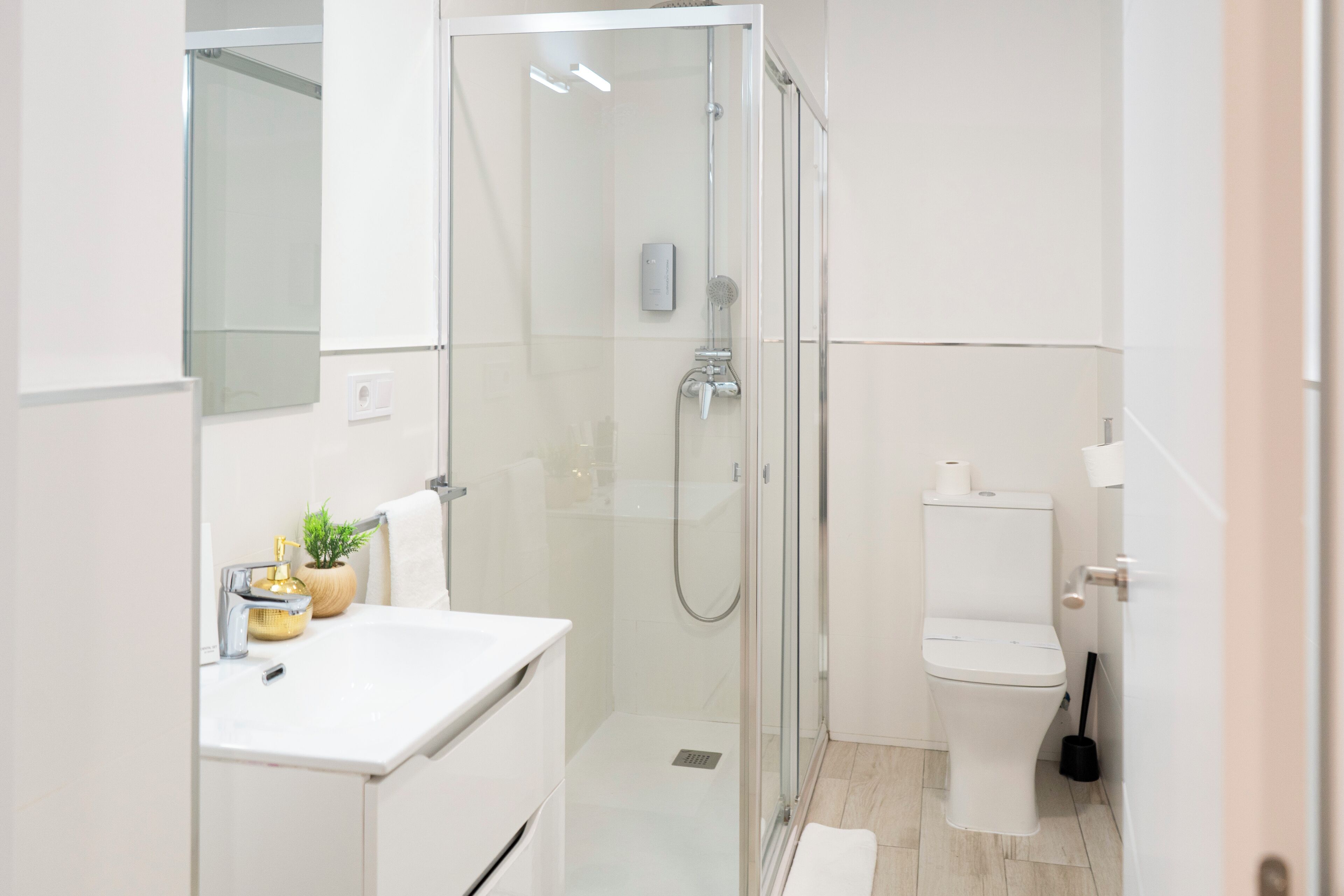 A modern bathroom with a glass-enclosed shower, a white sink with a gold faucet, and a toilet.