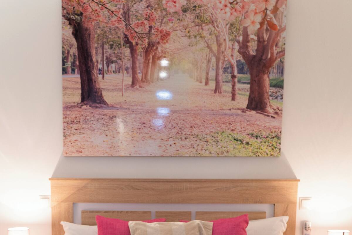 A hotel room with a large bed, two bedside tables, and a painting of a park.