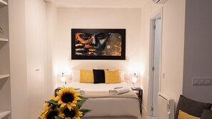 Hotellihuone, jossa on suuri sänky, kaksi yöpöytää valaisimineen, seinälle ripustettu taideteos ja maljakko täynnä auringonkukkia.