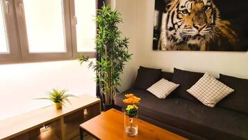 Una sala de estar con un sofá, una mesa de centro con un jarrón de flores, una planta en maceta y un cuadro de un tigre en la pared.