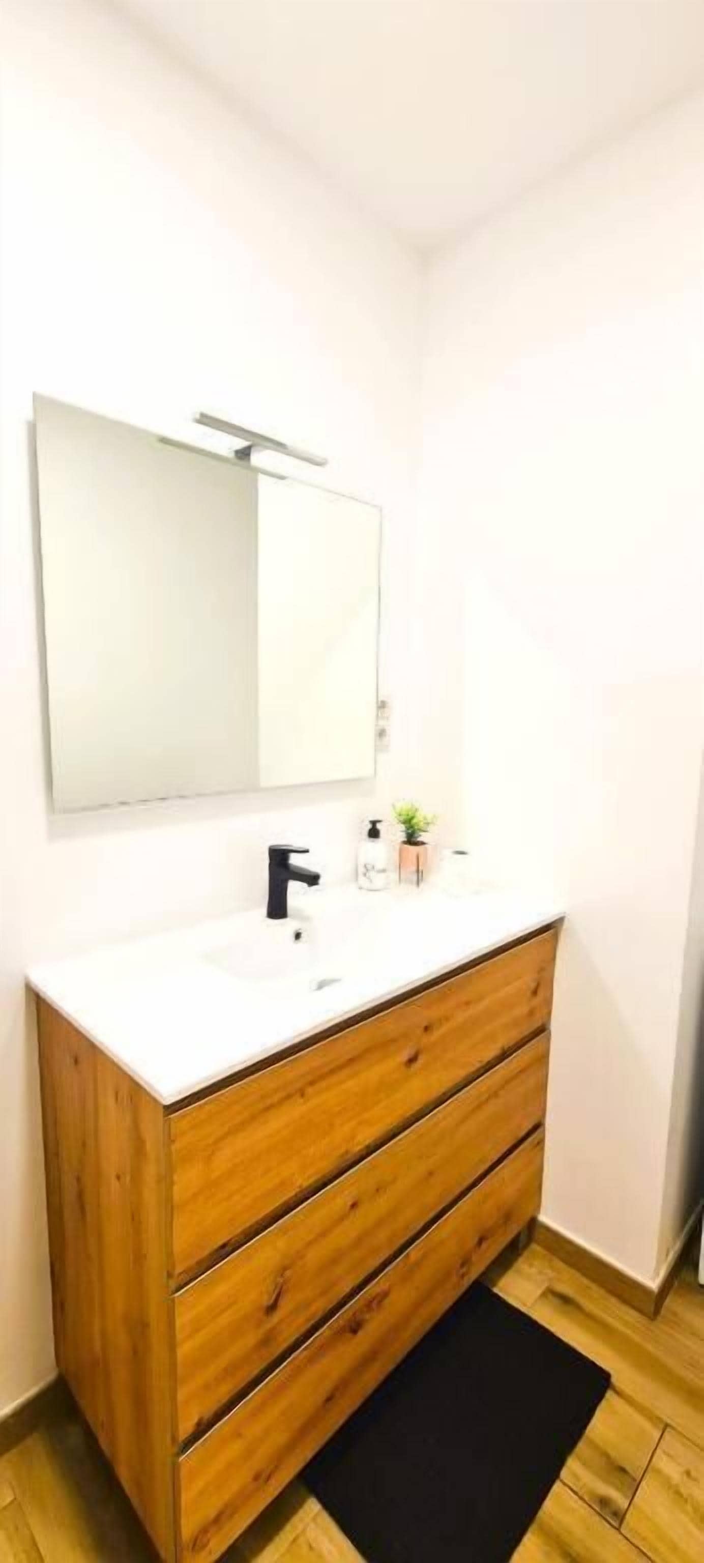 A bathroom with a white vanity, wooden cabinet, and a mirror.