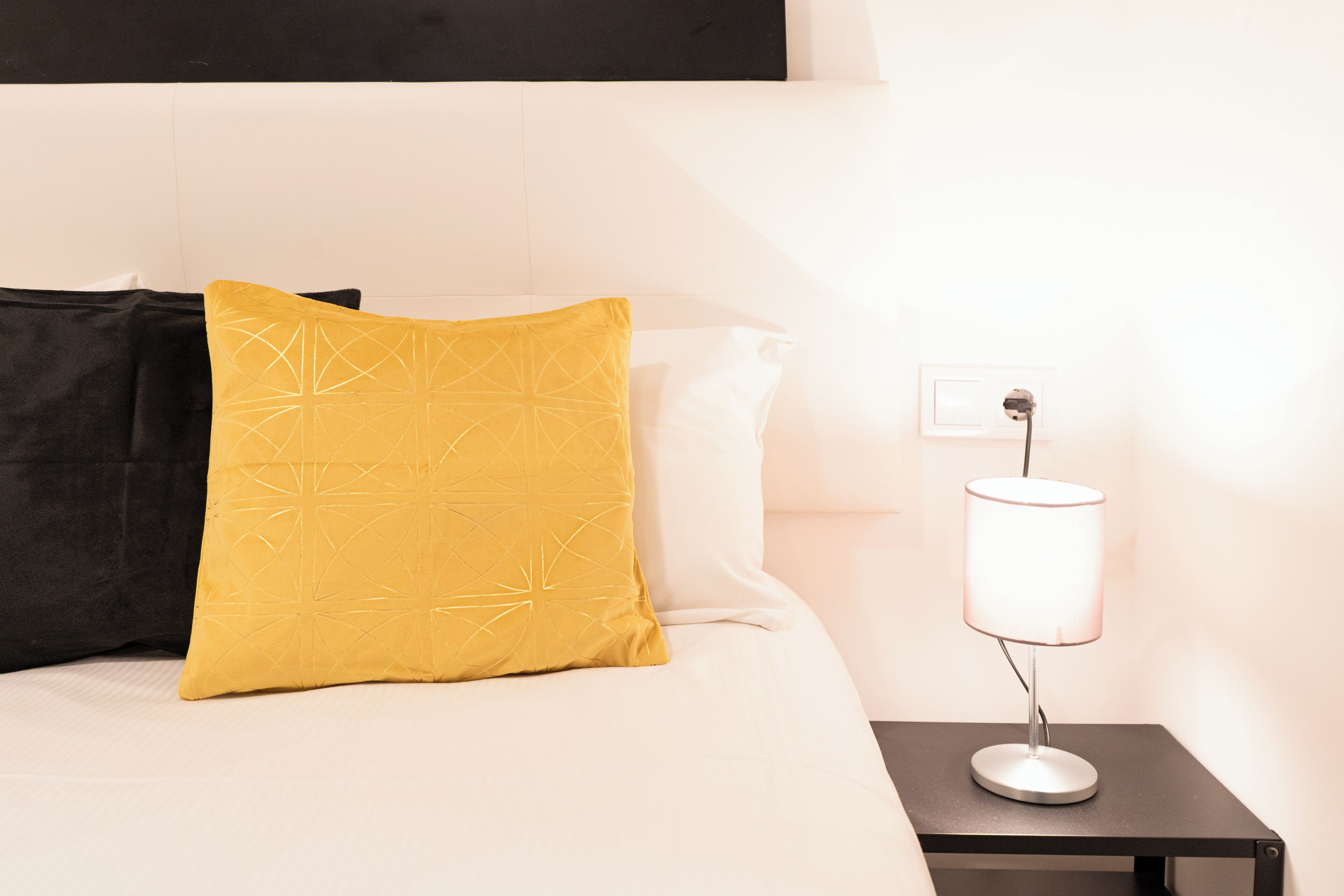 A bed with a black and yellow pillow, a white pillow, and a bedside table with a lamp.