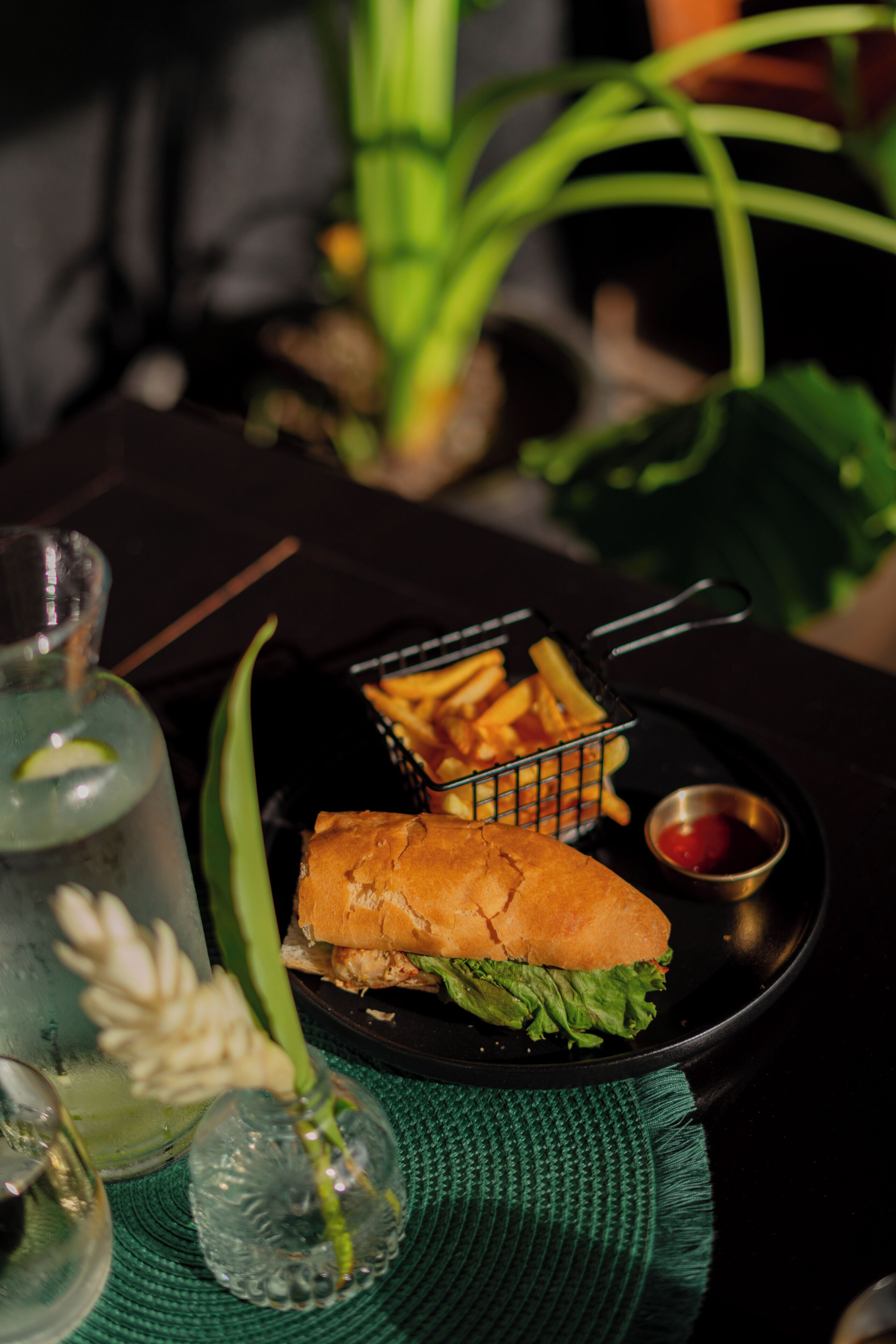 A meal consisting of a sandwich, fries, and a drink on a black plate with a green napkin underneath.