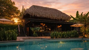 Eine Poolbar mit einem Reetdach, umgeben von tropischen Pflanzen und einem klaren Pool.
