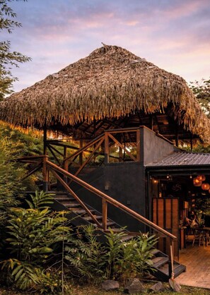 A thatched-roof structure with a staircase leading to an upper level, surrounded by lush greenery. - Jungle River Resort - Adults Only (Bahía Ballena)
