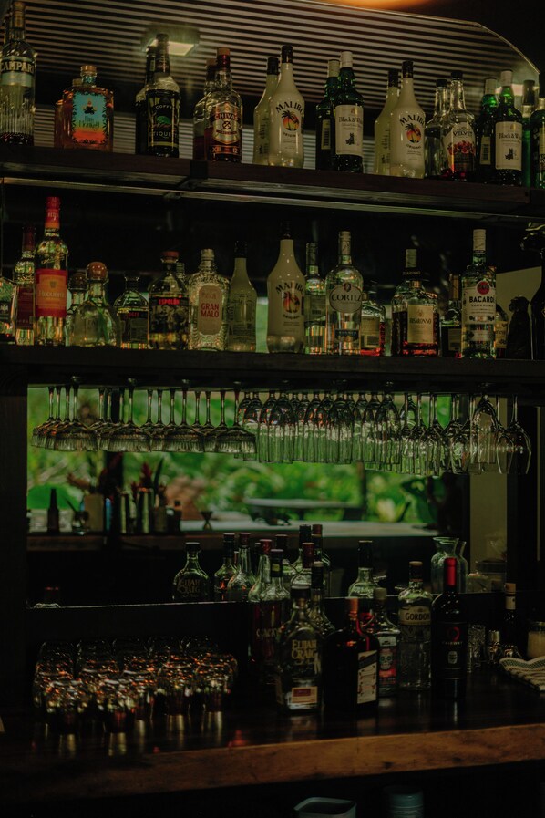 Un bar avec des étagères remplies de bouteilles d’alcool et une variété de verres suspendus au-dessus.