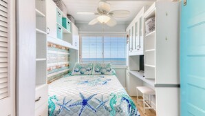 A bedroom with a bed, a ceiling fan, a window with blinds, and built-in storage units.