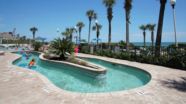 Ein Poolbereich mit Palmen und Blick aufs Meer.
