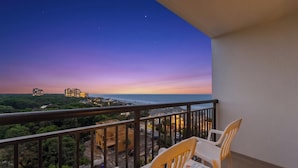 Ein Balkon mit Blick auf einen Sonnenuntergang über dem Meer, ein Tisch mit Stühlen und einer Zeitschrift.