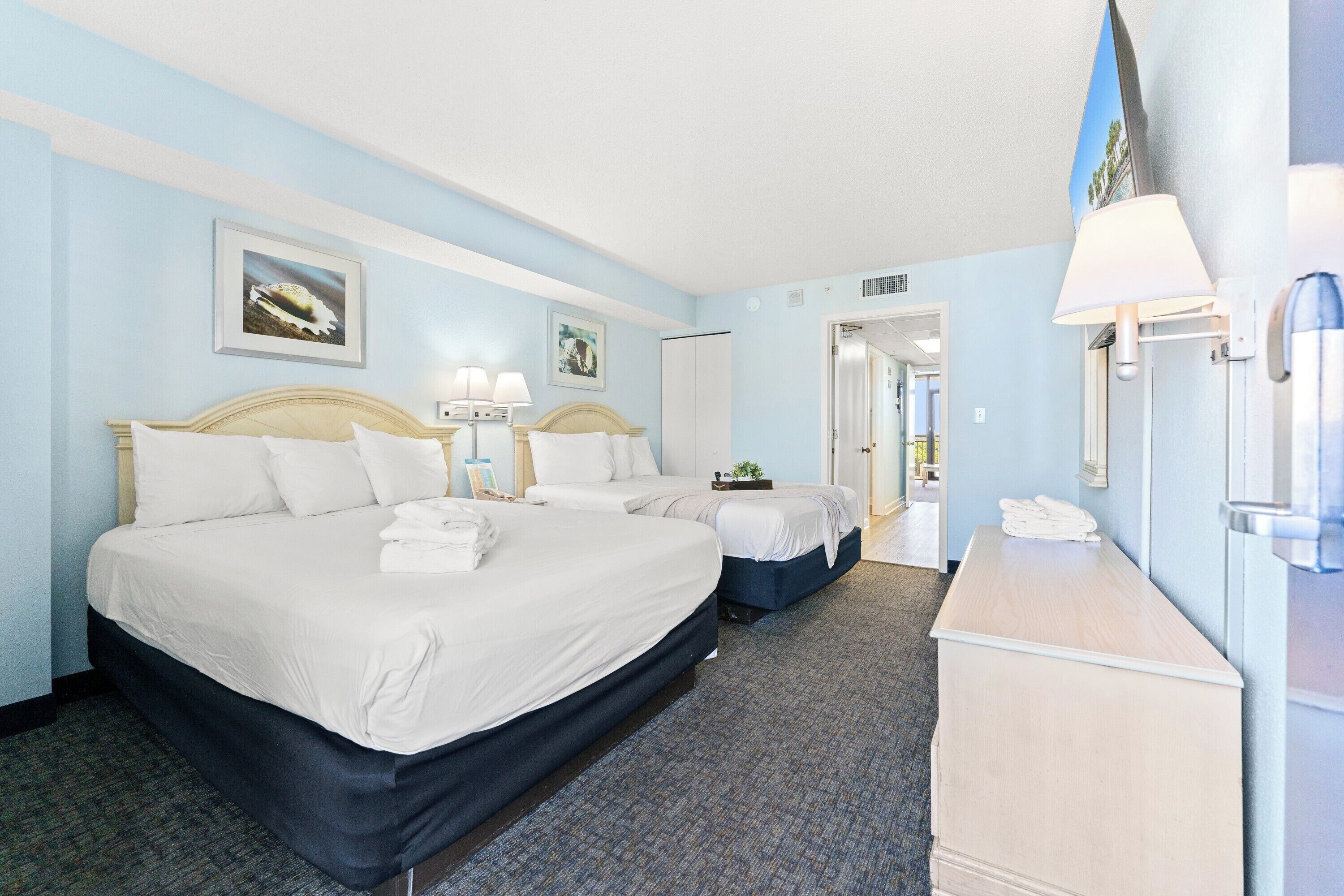 A hotel room with two beds, a desk, a mirror, and artwork on the walls.