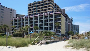 Ein mehrstöckiges Hotel mit Balkonen in der Nähe eines Strandes mit Sandweg und Palmen.