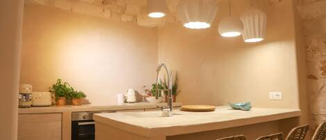 A kitchen with a central island, a built-in oven, and a sink. There are wicker chairs and a blue bowl on the island.