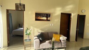 Ein Wohnzimmer mit einer Couch, einem kleinen Tisch mit Blumenvase, einem Gemälde an der Wand und einer Uhr.