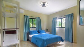 Ein Schlafzimmer mit Bett, Schreibtisch und Stuhl. Vor den Fenstern hängen Vorhänge.