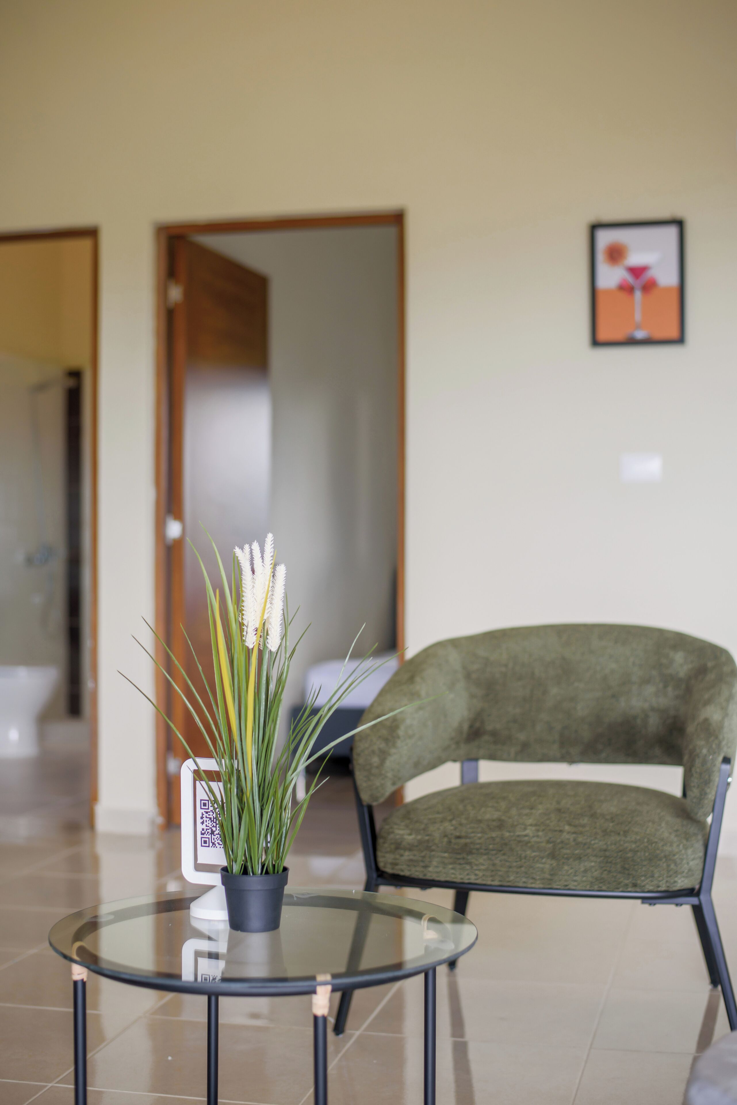 Una hall con un tavolo rotondo in vetro, una pianta in vaso, una poltrona rivestita in verde e un quadro appeso al muro.