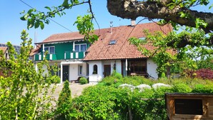 Ein zweigeschossiges Haus mit rotem Ziegeldach, einem Balkon und einem Garten mit einer Holzkonstruktion.