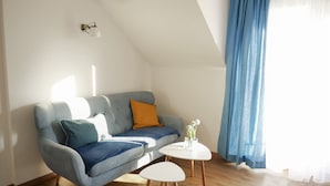 Un soggiorno moderno con un divano grigio, un piccolo tavolino bianco e una tenda blu.
