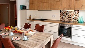 A modern kitchen with wooden cabinets, a built-in oven, and a dining table set with plates, cups, and a fruit bowl. - House Apple Blossom - No 3 (Langenargen)