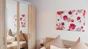 A bedroom with a wooden wardrobe, a bed with beige bedding, and a nightstand with a lamp. - House Apple Blossom - No 3 (Langenargen)