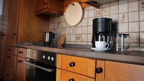 A kitchen with wooden cabinets, a stainless steel stove, a coffee maker, a cup, and a glass pitcher on the counter. - House Apple Blossom - No 4 (Langenargen)