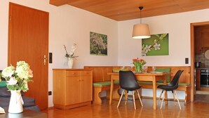 A dining area with wooden furniture, a bench, and a table with chairs. There is a wooden cabinet and a vase with flowers on the table. - House Apple Blossom - No 4 (Langenargen)