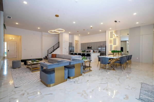 A spacious living area with a modern sofa, a dining table with chairs, and a kitchen in the background.