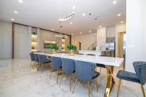A modern kitchen with stainless steel appliances, a white countertop, and a dining area with a marble floor and blue chairs.
