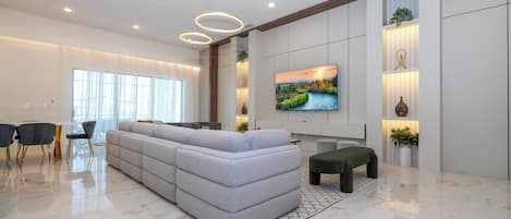 Una sala de estar moderna con un sofá seccional, un televisor de pantalla plana montado en la pared y un comedor con mesa y sillas.