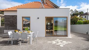 A modern house with a stone wall, a satellite dish, a dining area with a table and chairs, and a large sliding glass door leading to a kitchen. - Exceptional stone character house |Chalet Prazeres (Prazeres)