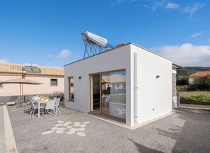 A modern white building with a satellite dish, a patio with a table and chairs, and a glass door. - Exceptional stone character house |Chalet Prazeres (Prazeres)