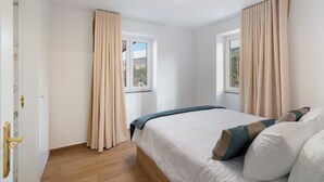 A bedroom with a bed, beige curtains, a window, and a ceiling light. - Exceptional stone character house |Chalet Prazeres (Prazeres)