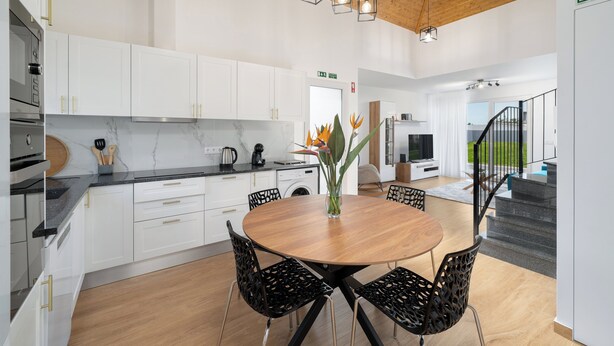 A modern kitchen with white cabinets, a wooden dining table, and black chairs. - Exceptional stone character house |Chalet Prazeres (Prazeres)