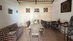 Un'ampia zona giorno con soffitto alto, un tavolo da pranzo circondato da sedie, un divano e un angolo cottura con tavolo e sedute.