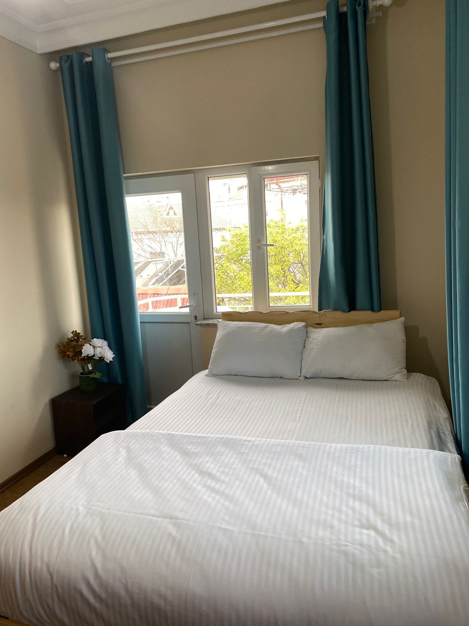 A bedroom with a bed, a window with curtains, and a nightstand with a vase of flowers.