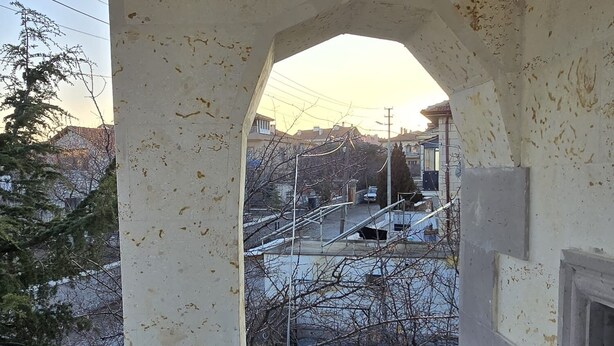 Un balcón con vista a una zona residencial, una silla de mimbre y un banco acolchado.