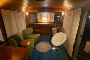 A compact living space with a sofa, armchair, small round table, and a bar area with a window. - 1951 Spartan Aircraft Cottage w/AC - Durham, NC (Durham)