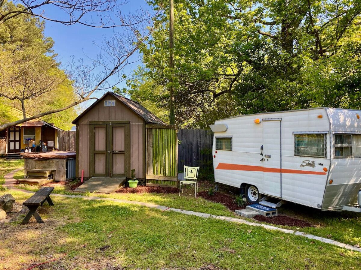 A wooden shed, a picnic table, and a white RV with orange stripes in a backyard.