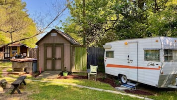 A wooden shed, a picnic table, and a white RV with orange stripes in a backyard.