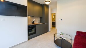 Una cocina moderna con armarios oscuros, horno empotrado y cafetera. Hay una mesa de vidrio con un control remoto y una silla roja.