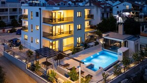 Un edificio moderno de varios pisos con balcones, piscina y telón de fondo montañoso.