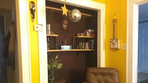 Une pièce avec un fauteuil en cuir marron, une bibliothèque remplie de divers objets, une boule à facettes et une décoration en forme d’étoile.