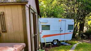 Une terrasse en bois mène à un espace extérieur abrité où est garé un camping-car blanc.