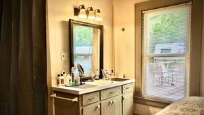 Une salle de bain avec un lavabo, un miroir et des stores aux fenêtres.